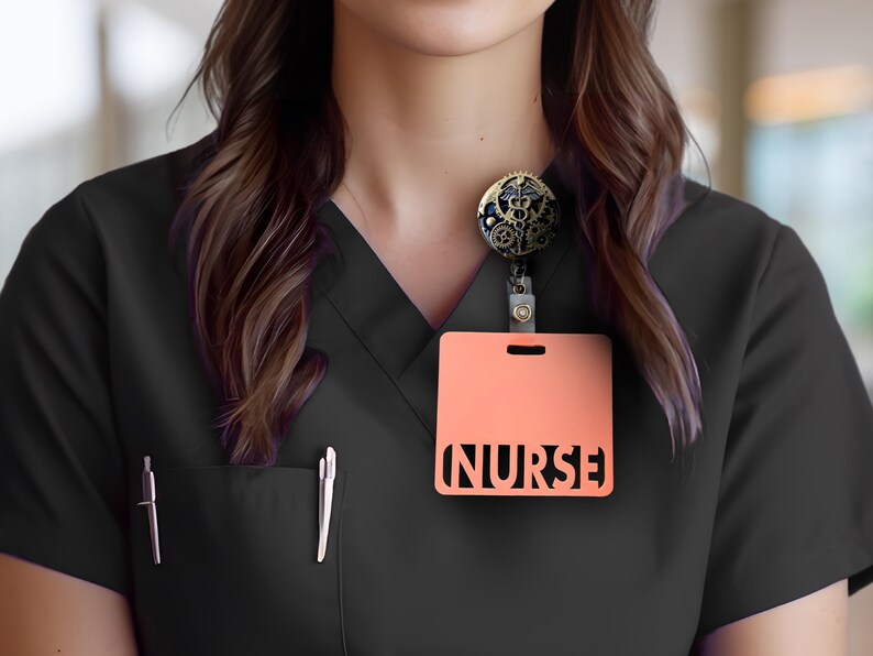 Puede incluir: Top de uniforme negro con un portatarjetas de color melocot&oacute;n. El portatarjetas tiene la palabra "NURSE" recortada. Se adjunta un carrete de insignia decorativo con engranajes y s&iacute;mbolos m&eacute;dicos. Dos bol&iacute;grafos est&aacute;n en el bolsillo.