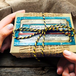 A pair of hands holding a small, brown box with a blue and yellow striped ribbon tied around it.