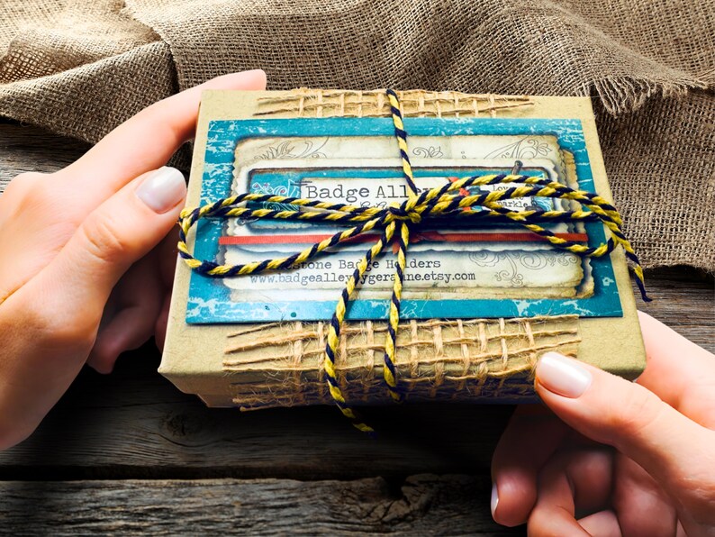 A pair of hands holding a small, brown box with a blue and yellow striped ribbon tied around it.