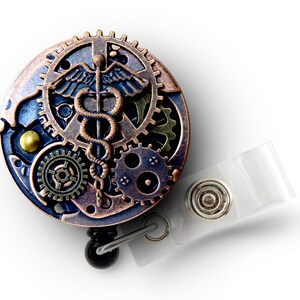 May include: A steampunk-style badge reel with a medical caduceus symbol. The round reel features bronze, copper, and blue gears and accents. A clear plastic strap and metal snap are attached for securing the badge.