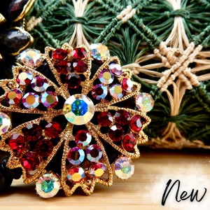 May include: A gold-tone flower-shaped badge holder with red and iridescent rhinestones. The badge holder is on a wooden surface with the word "New!" written in black.