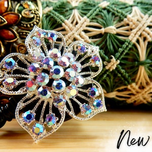 May include: A silver flower-shaped badge reel with iridescent rhinestones. The reel is attached to a black retractable cord. The word "New!" is written in black on a wooden surface.