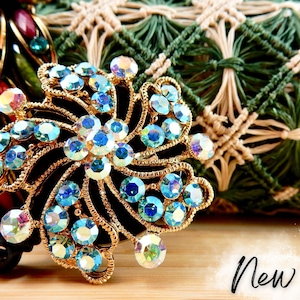 May include: A gold-tone, decorative, jeweled flower-shaped badge holder with blue iridescent rhinestones. The badge holder is attached to a black retractable badge reel.