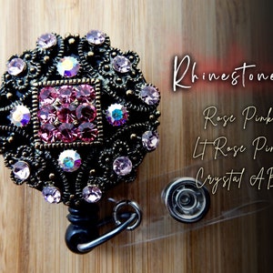 Pu&ograve; includere: Un porta badge retrattile nero con un ciondolo in metallo decorativo che presenta un design quadrato con strass rosa, rosa chiaro e AB trasparenti. Il ciondolo &egrave; circondato da una cornice in metallo decorativa con un motivo floreale.