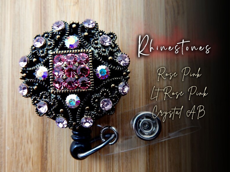 Pu&ograve; includere: Un porta badge retrattile nero con un ciondolo in metallo decorativo che presenta un design quadrato con strass rosa, rosa chiaro e AB trasparenti. Il ciondolo &egrave; circondato da una cornice in metallo decorativa con un motivo floreale.