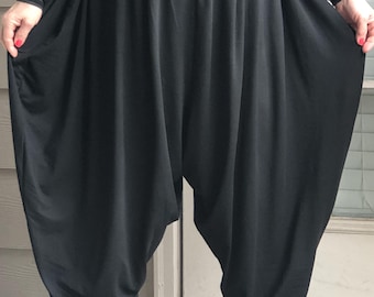May include: Black harem pants with a gathered elastic waistband and ankle cuffs. The pants have a loose, flowing design with a voluminous silhouette. The model is wearing a striped long-sleeve shirt and black boots.