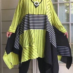 May include: A long-sleeved tunic dress featuring a vibrant lime green base with a textured vertical stripe pattern. The garment includes contrasting black and white horizontal striped panels across the midsection and solid black side panels.