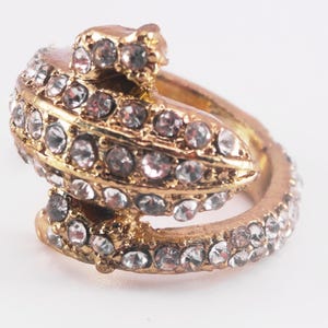 May include: A gold ring featuring a clear crystal design shaped like a curled up lizard.
