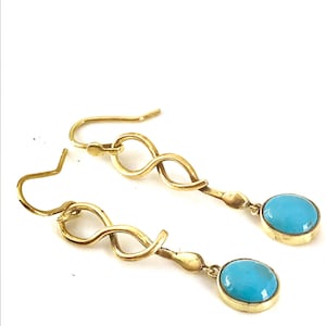 May include: A pair of gold-coloured earrings featuring turquoise stones. The earrings have an infinity symbol design and a hook closure. The oval-shaped turquoise stones are set in a gold bezel.