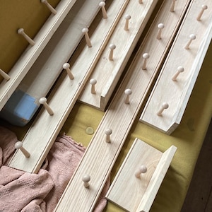 Puede incluir: Conjunto de seis percheros de madera con clavijas redondeadas. Los percheros son de madera clara y tienen un acabado natural.