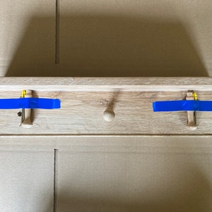 Puede incluir: Una estanter&iacute;a de madera con dos ganchos y un pomo en el centro. La estanter&iacute;a est&aacute; fijada a la pared con cinta de pintor azul.