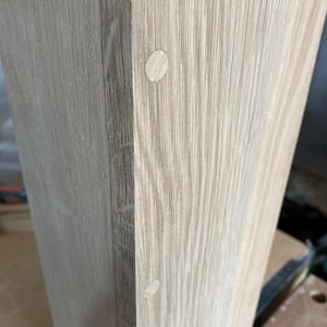 Puede incluir: Primer plano de una superficie de madera clara con dos peque&ntilde;os tapones redondos de madera blanca. Los tapones est&aacute;n espaciados uniformemente y est&aacute;n al ras con la superficie.