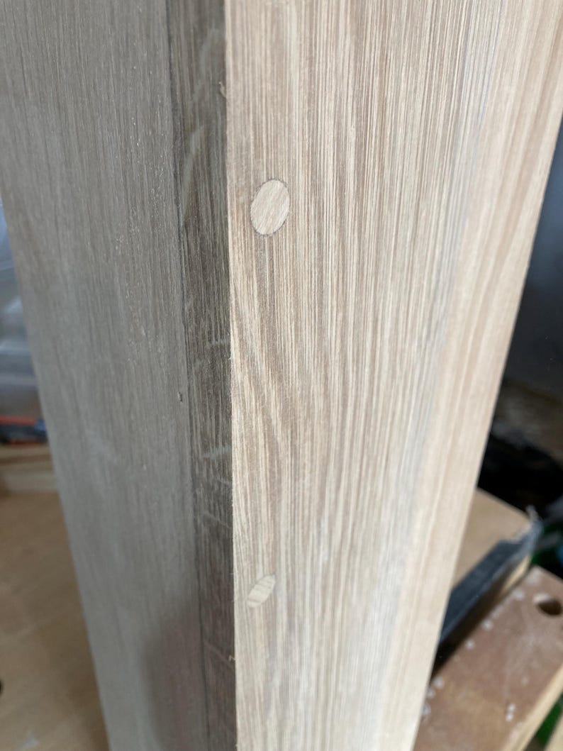 Puede incluir: Primer plano de una superficie de madera clara con dos peque&ntilde;os tapones redondos de madera blanca. Los tapones est&aacute;n espaciados uniformemente y est&aacute;n al ras con la superficie.