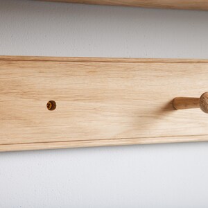 Puede incluir: Un primer plano de una estanter&iacute;a de madera con un solo gancho de madera. La estanter&iacute;a est&aacute; hecha de madera de color claro y tiene un acabado liso. El gancho est&aacute; fijado a la estanter&iacute;a con un tornillo.