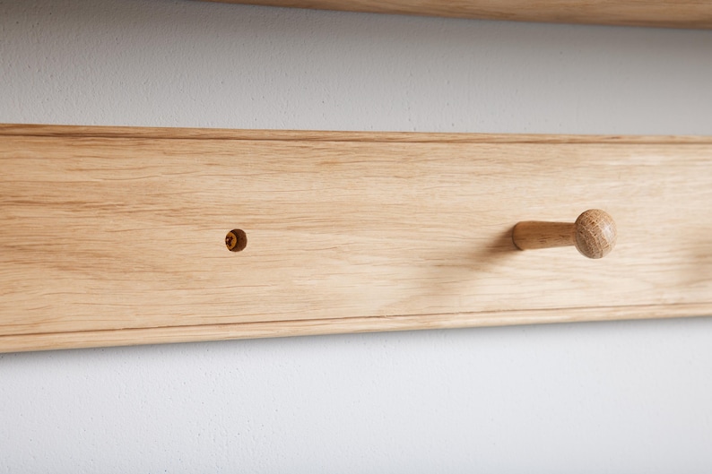 Puede incluir: Un primer plano de una estanter&iacute;a de madera con un solo gancho de madera. La estanter&iacute;a est&aacute; hecha de madera de color claro y tiene un acabado liso. El gancho est&aacute; fijado a la estanter&iacute;a con un tornillo.