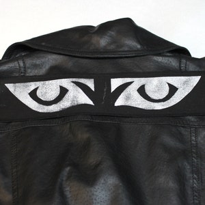 Könnte beinhalten: Schwarze Lederjacke mit einem weißen Augenfleck, der auf der Rückseite aufgenäht ist.
