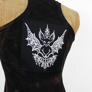 Könnte beinhalten: Schwarzes Tanktop mit einem schwarzen und weißen gestickten Fledermaus-Design auf der Rückseite.