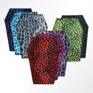 Könnte beinhalten: Eine Sammlung von sieben Sarg-förmigen Stoffstücken mit Leopardenmuster. Die Farben umfassen Blau, Hellblau, Grau, Rot, Rosa, Lila, Grün und Schwarz. Jedes Stück hat eine kontrastierende farbige Umrandung.