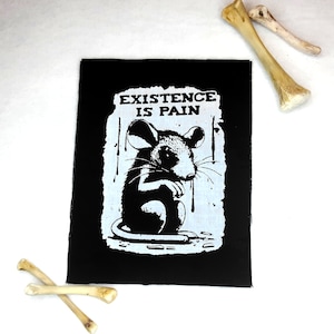 Könnte beinhalten: Schwarz-weißes Bügeleisen-Patch mit einem abgenutzten weißen Hintergrund. Das Patch zeigt eine Comic-Maus mit dem Text "EXISTENCE IS PAIN" darüber.