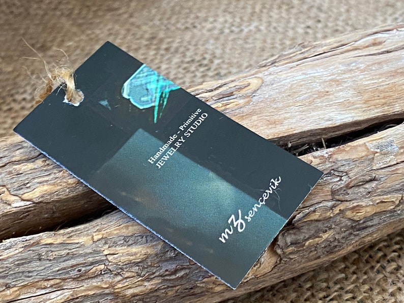 K&ouml;nnte beinhalten: Ein schwarzes Etikett mit wei&szlig;em Text, auf dem "Handmade - Primitive Jewelry Studio" und "mJ sencenik" steht. Das Etikett ist mit einer Schnur gebunden und liegt auf einem St&uuml;ck Treibholz.