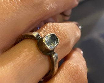 May include: A silver ring with a clear gemstone set in a textured band.