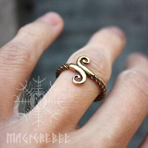 May include: A gold-toned ring with a twisted band and a stylized double-spiral design.