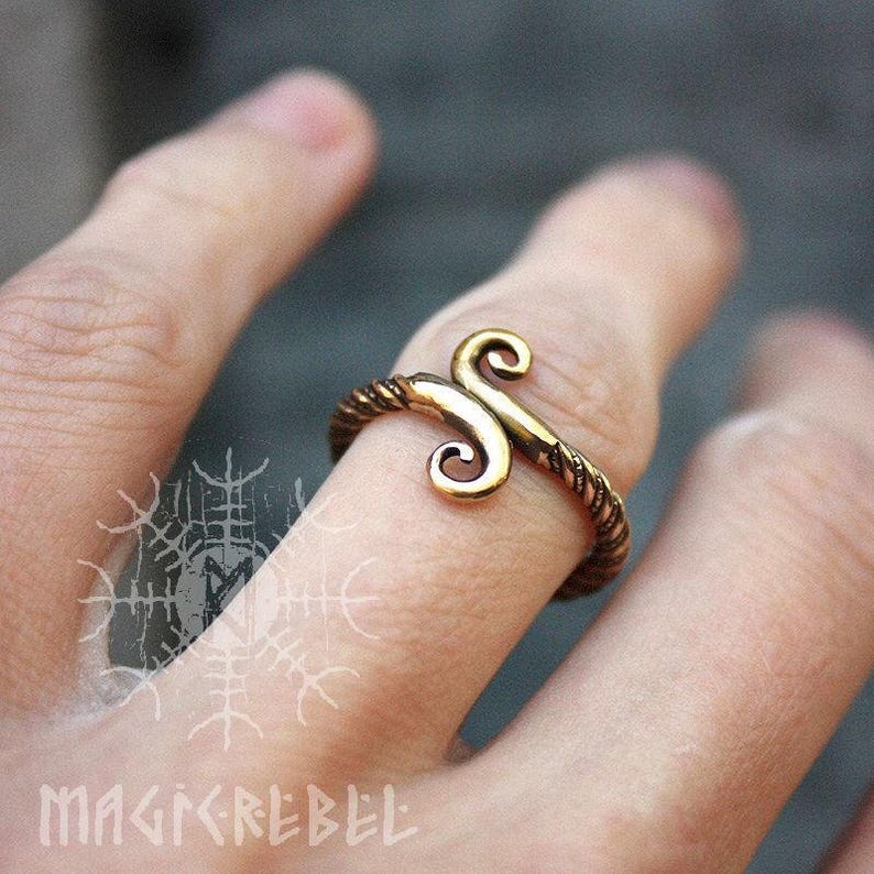 May include: A gold-toned ring with a twisted band and a stylized double-spiral design.