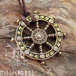Puede incluir: Colgante de color bronce con un dise&ntilde;o de rueda con intrincados patrones y un medall&oacute;n central. El colgante est&aacute; suspendido de un cord&oacute;n marr&oacute;n. La palabra "MAGICREBEL" es visible en la parte inferior de la imagen.