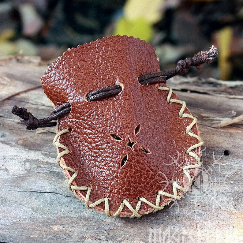 May include: A small brown leather pouch with a drawstring closure and a decorative stitch pattern around the edge. The pouch has a cut-out design in the center.