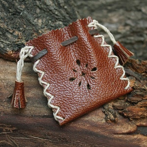 May include: A small brown leather pouch with a white drawstring and tassel. The pouch has a decorative cut-out design and is perfect for holding small items.