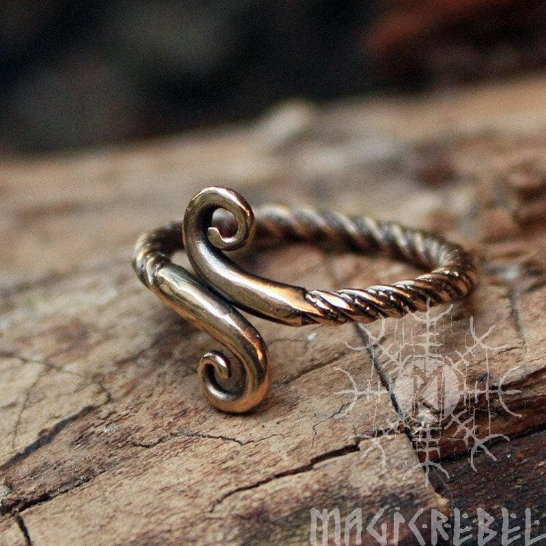 May include: A bronze ring with a twisted band and a decorative swirl design. The ring is handcrafted and has a rustic, antique look.