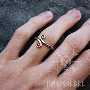 May include: A bronze ring with a twisted band and a double spiral design. The ring is worn on a person's finger.