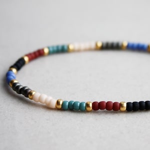 Può includere: Un braccialetto colorato con una miscela di perline blu, rosse, nere, bianche e dorate.