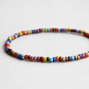 May include: A circular bracelet composed of small, matte-finish seed beads in a variety of colors including red, blue, yellow, green, orange, and grey. The beads are strung together in a continuous loop, creating a simple, thin, and flexible band.