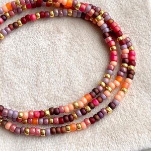 May include: Multi-strand beaded bracelet with a mix of pink, purple, orange, and gold beads.