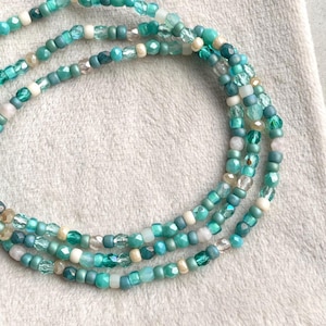 Könnte beinhalten: Drei Stränge aus Perlen-Schmuck in Türkis-, Türkis- und Weißtönen. Die Perlen sind in verschiedenen Formen und Größen gehalten, was einen strukturierten Look erzeugt. Der Schmuck ist wahrscheinlich eine Halskette oder ein Armband.