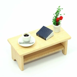 May include: A miniature wooden table with a shelf, a cup of coffee, a small book, and a potted plant with red flowers.