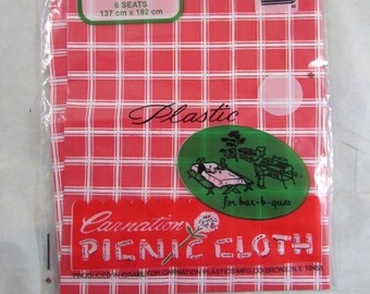 May include: A red and white checkered plastic picnic tablecloth with the words "Carnation Picnic Cloth" and "Easy Care 54" x 72" 6 Seats 137 cm x 182 cm" printed on it. The tablecloth is packaged in a clear plastic bag.