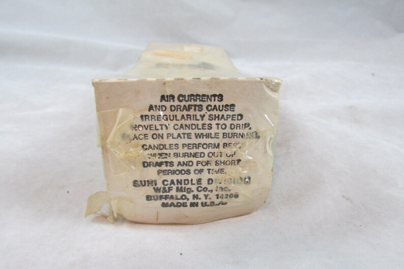 May include: A white box with black text explaining that air currents and drafts can cause irregularly shaped novelty candles to drip. The box also states that the candles perform best when burned out of drafts and for short periods of time. The box is labeled "Suni Candle Division, W&F Mig. Co., Inc., Buffalo, N.Y. 14206, Made in U.S.A."