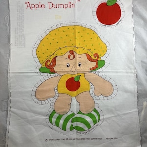 May include: A vintage Apple Dumplin' fabric panel featuring a cartoon character with a yellow hat, red hair, and a yellow outfit with an apple. The design includes an apple illustration and the text "Apple Dumplin'" in red. The panel is white with a printed design.