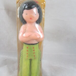 May include: A plastic doll figurine of a Native American person wearing a green and red outfit with fringe. The doll is packaged in clear plastic.