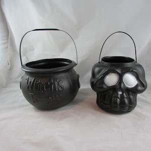 May include: Two black plastic Halloween trick-or-treat buckets. One is shaped like a cauldron with the words "Witch's Brew" on the side. The other is shaped like a skull with white eyes.