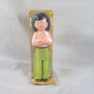 May include: A plastic doll figurine of a person wearing a green outfit with red accents and fringe. The doll is packaged in a clear plastic bag with a yellow cardboard backing.