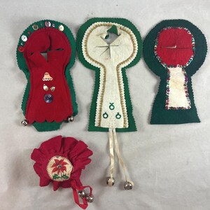 May include: A collection of vintage Christmas ornaments. The ornaments are made of felt in red, green, and white. Some have sequins, bells, and embroidered details. One ornament is a red rosette with a poinsettia design.