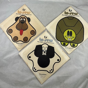 May include: Three sewing patterns featuring a monkey, turtle, and dog. Each pattern is printed on a white card with a brown border and the text "to-sew The simple way to learn to sew." The monkey pattern is brown with black eyes and a red tongue. The turtle pattern is green with yellow eyes and a yellow smile. The dog pattern is black and white with black eyes and a black nose.