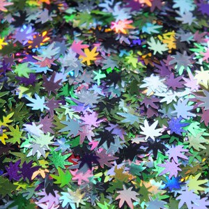 Puede incluir: Primer plano de purpurina holográfica iridiscente en forma de hojas de marihuana. La purpurina es una mezcla de verde, azul, morado y rosa.