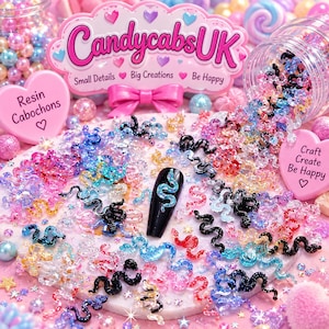 Puede incluir: Una colección de pequeños cabujones de resina con forma de serpiente, brillantes y de varios colores, incluyendo azul, rosa, negro y transparente. Una punta de uña negra muestra un cabujón de serpiente azul. La marca CandycabsUK es visible al fondo.