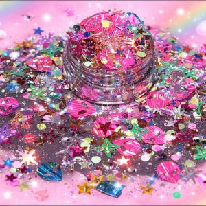 May include: A clear glass jar filled with pink, silver, and iridescent glitter. The glitter is scattered around the jar on a pink surface, with star, circle, and butterfly shapes. The background has a rainbow and clouds.