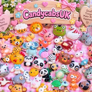 Puede incluir: Una colección de pequeños cabujones de resina coloridos y planos con varios animales de dibujos animados, incluyendo pandas, leones, ranas y elefantes. Un letrero de madera con el texto CandycabsUK y Small Things Make Big Happiness es visible.