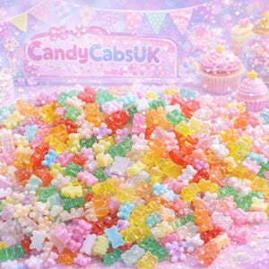 Op de afbeelding: Een kleurrijk assortiment gummy snoepjes in diverse vormen en kleuren, waaronder beren en bloemen, is verspreid over een glinsterend oppervlak. De afbeelding toont een bord met de tekst "CandyCabsUK" en decoratieve cupcakes en lollies.